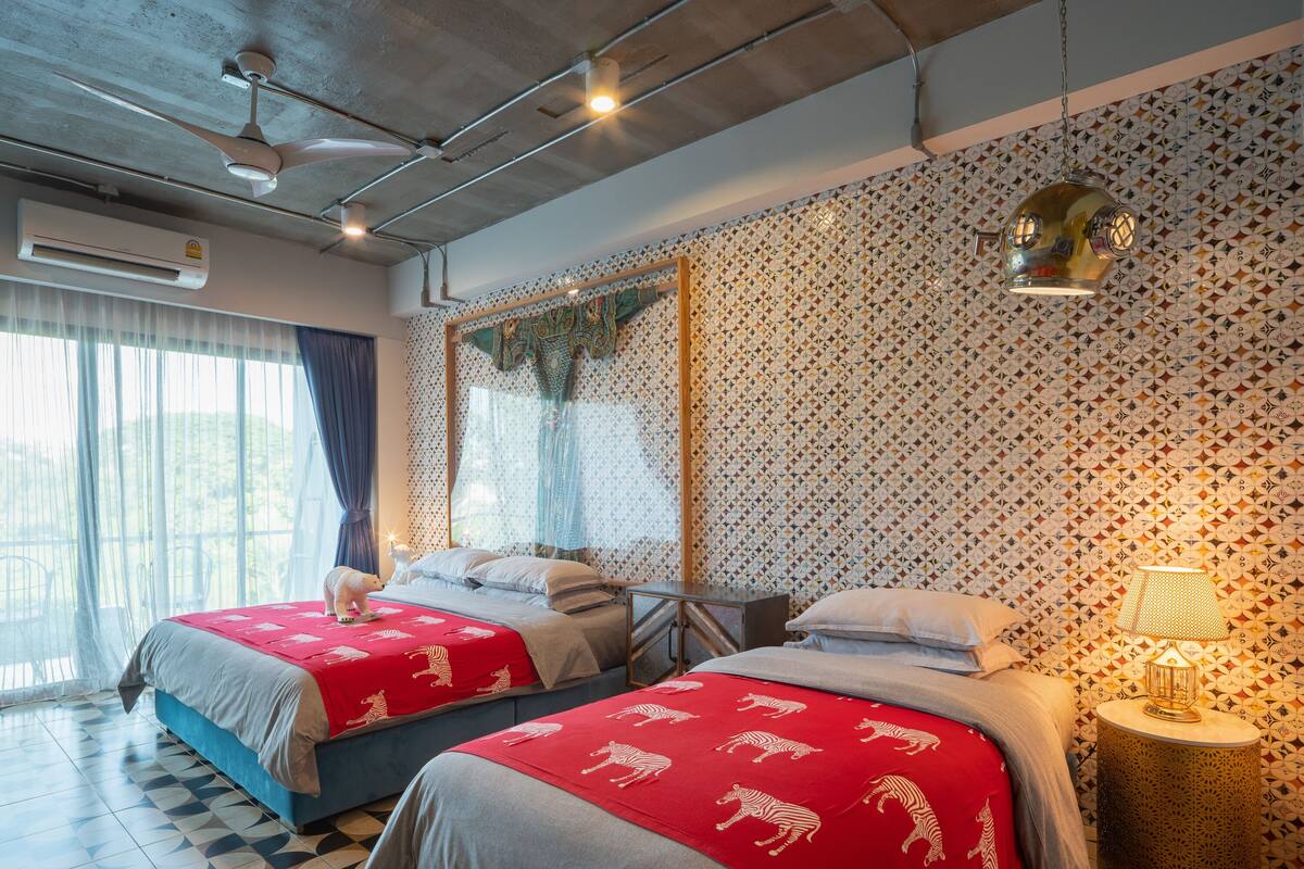 Une chambre d’hôtel avec deux lits, un mur décoré de motifs, un ventilateur de plafond et une fenêtre avec des rideaux.