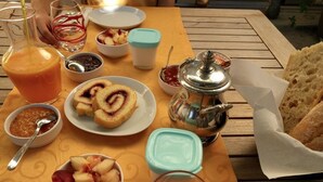Une table de petit-déjeuner avec divers aliments, notamment un verre de jus d’orange, une assiette de viennoiseries et une théière.