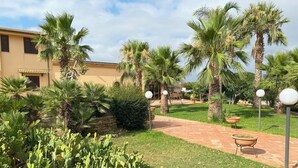 A courtyard with palm trees, a cactus garden, and a patio area with outdoor furniture. - Agriturismo Le Arcate (Marsala)