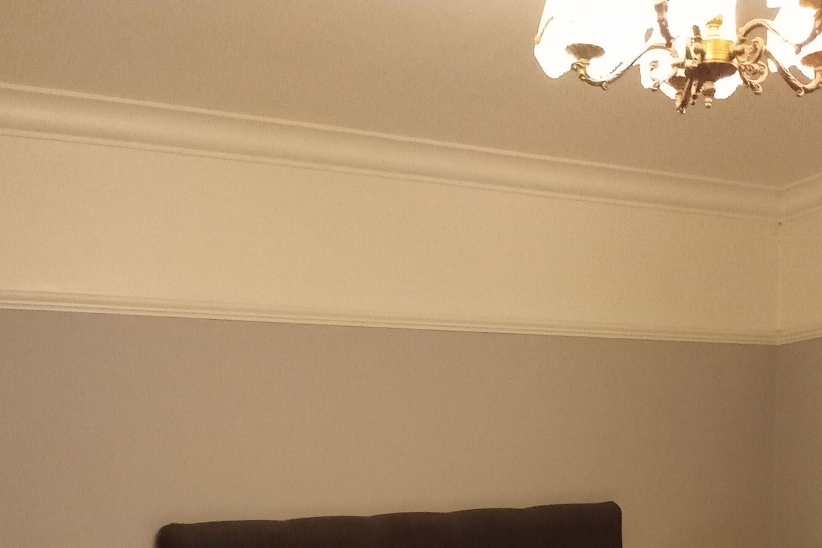 Cama bem arrumada com cabeceira escura, duas mesas de cabeceira com luminárias e um lustre acima.