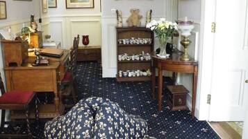 A room with a round, floral-patterned sofa, a chandelier, a deer skull on the wall, and a collection of framed pictures.