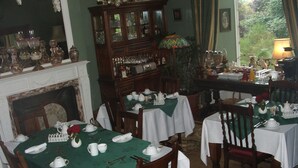 A dining room with multiple tables set for tea, a fireplace, and a large wooden cabinet with glass doors. - Disblair House (Aberdeen)