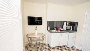 A compact kitchen with a small dining table, a TV mounted above it, and a microwave on the counter.