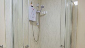 A glass-enclosed shower stall with a handheld showerhead and a wall-mounted faucet.