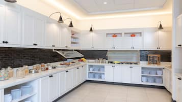 A modern kitchen with white cabinets, a brick backsplash, and a breakfast bar with various food items.