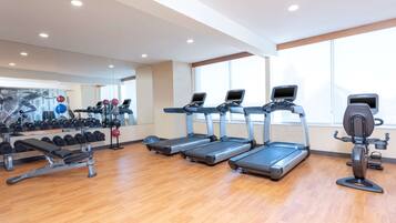 Un gimnasio con cintas de correr, mancuernas y un banco.