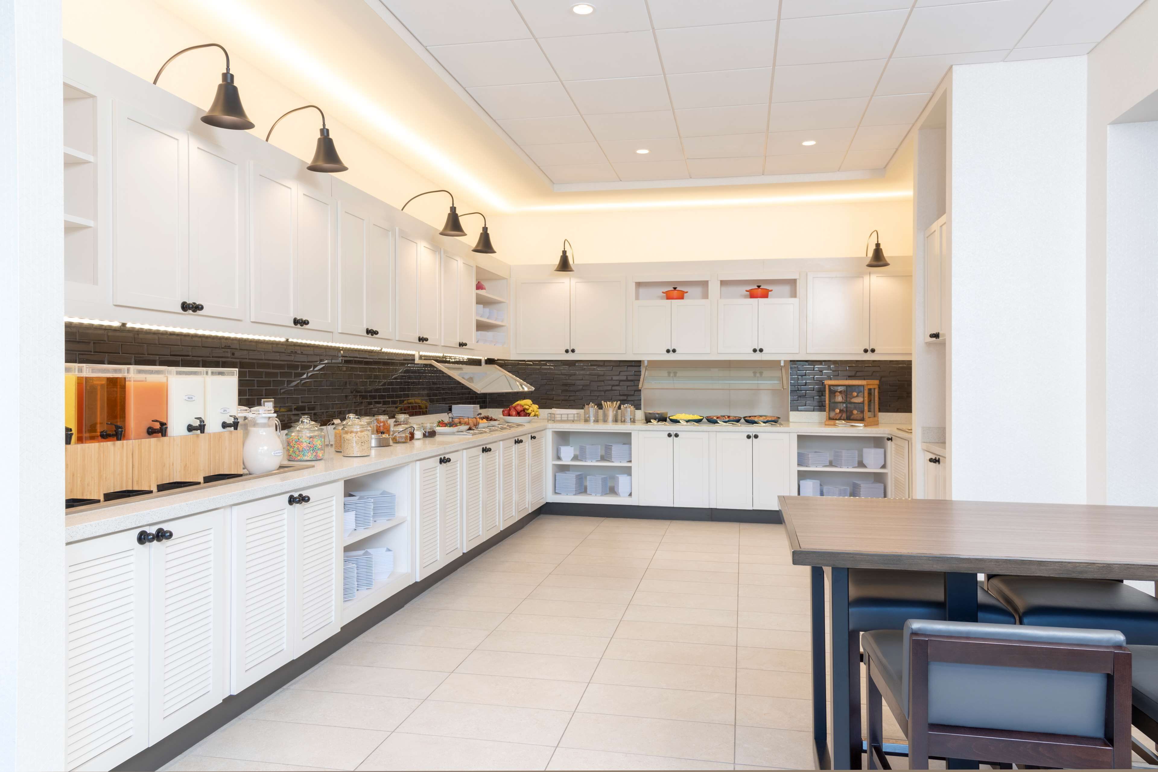 A modern kitchen with white cabinets, black pendant lights, and a central island.