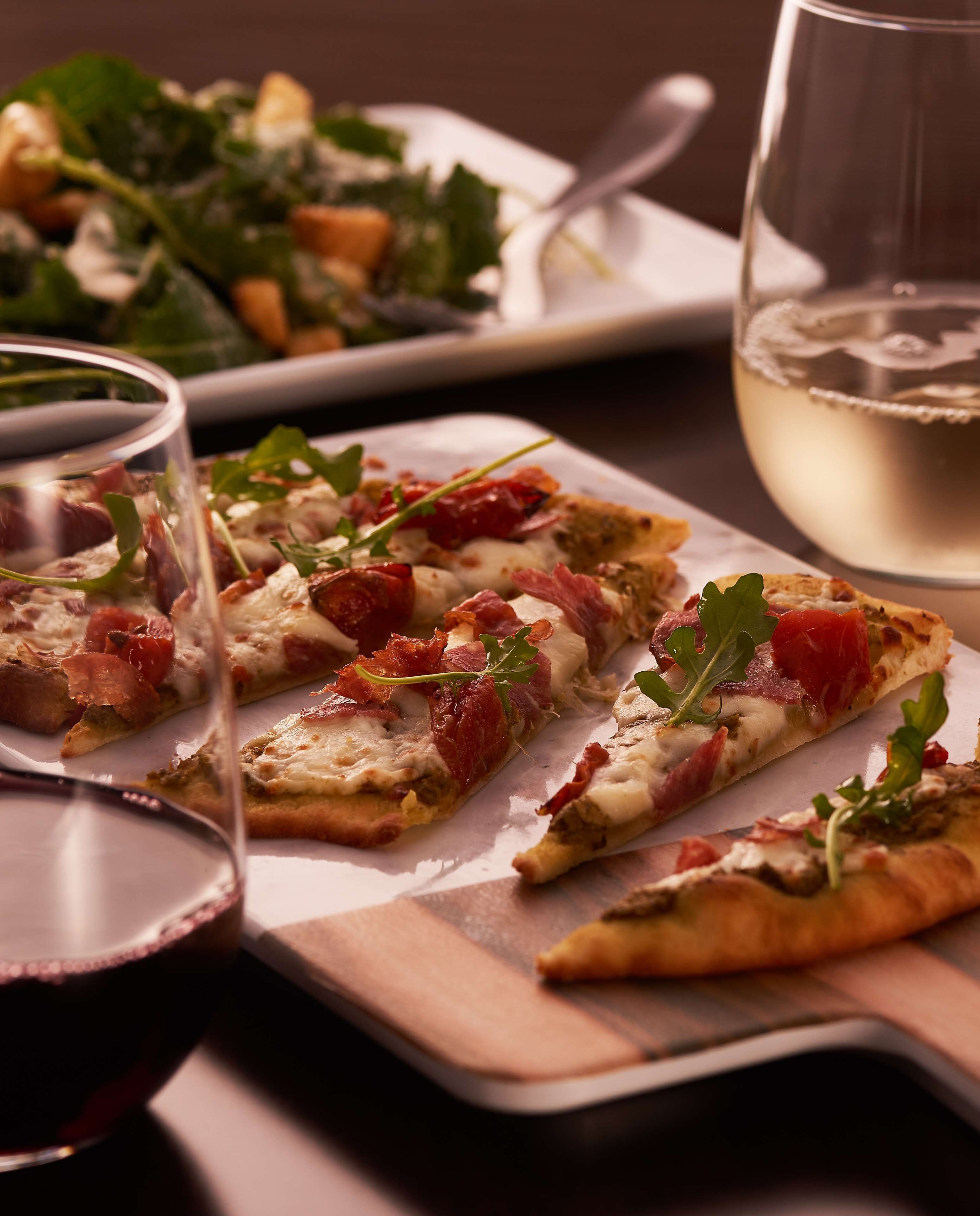 A table with a plate of pizza slices, a glass of white wine, and a glass of red wine.