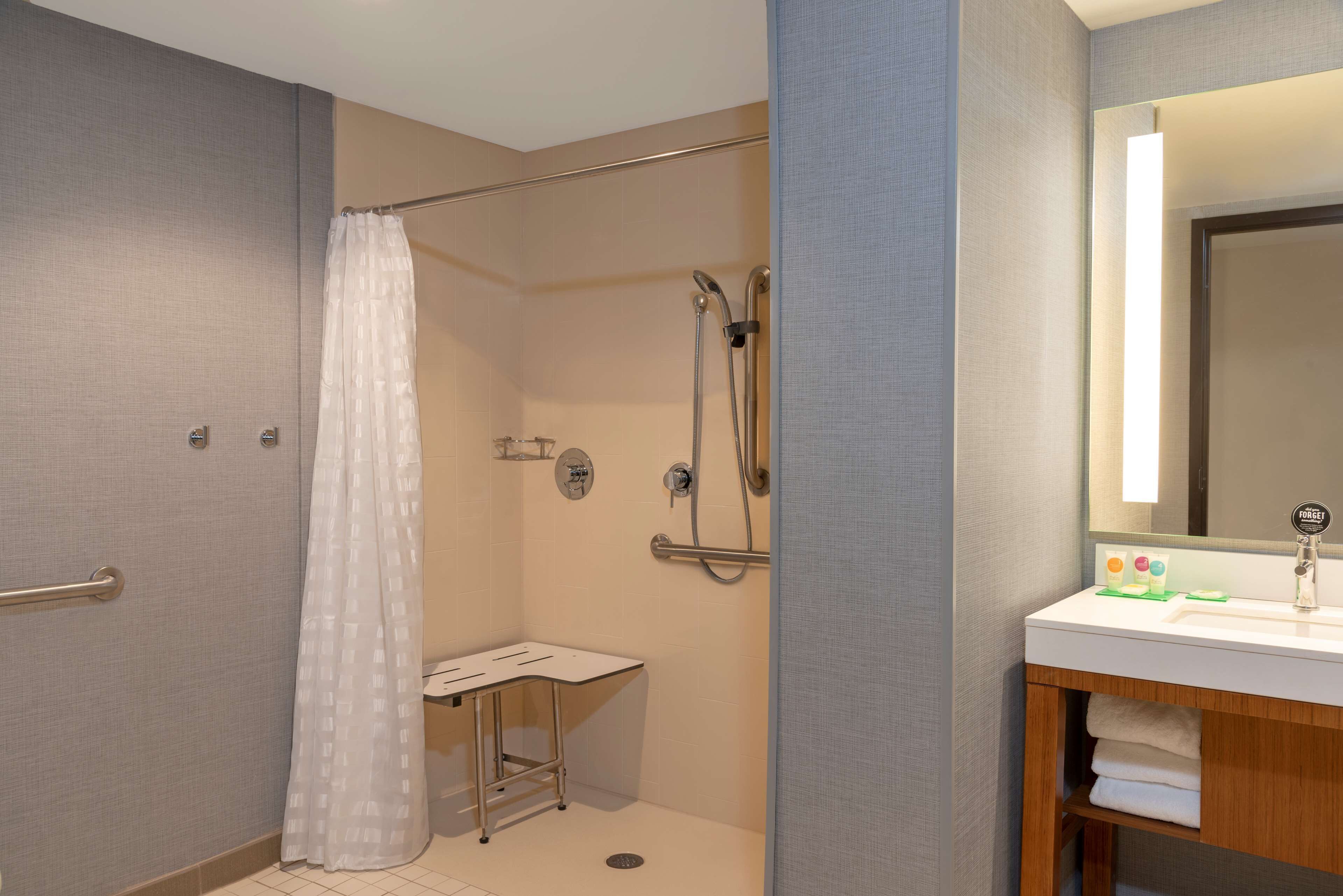 A modern bathroom with a shower, a small vanity with a mirror, and a towel rack.