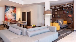 A modern living room with a gray sofa, yellow chairs, a wooden coffee table, and a large abstract painting. - Hyatt Place Detroit Royal Oak (Royal Oak)