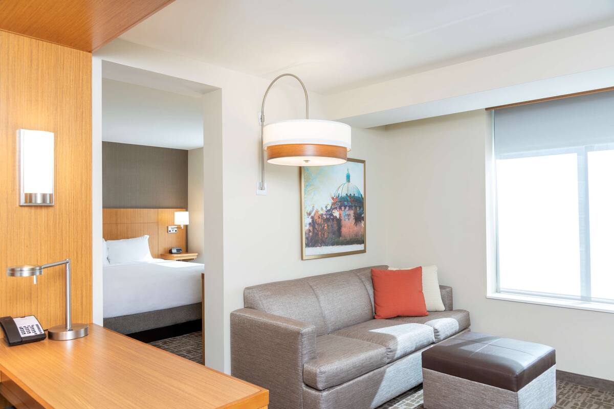 A hotel room with a bed, a sofa, a desk, a lamp, and a painting on the wall.