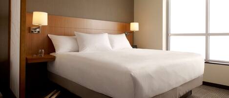 A hotel room with a large bed, two bedside lamps, a wooden headboard, and a large window.