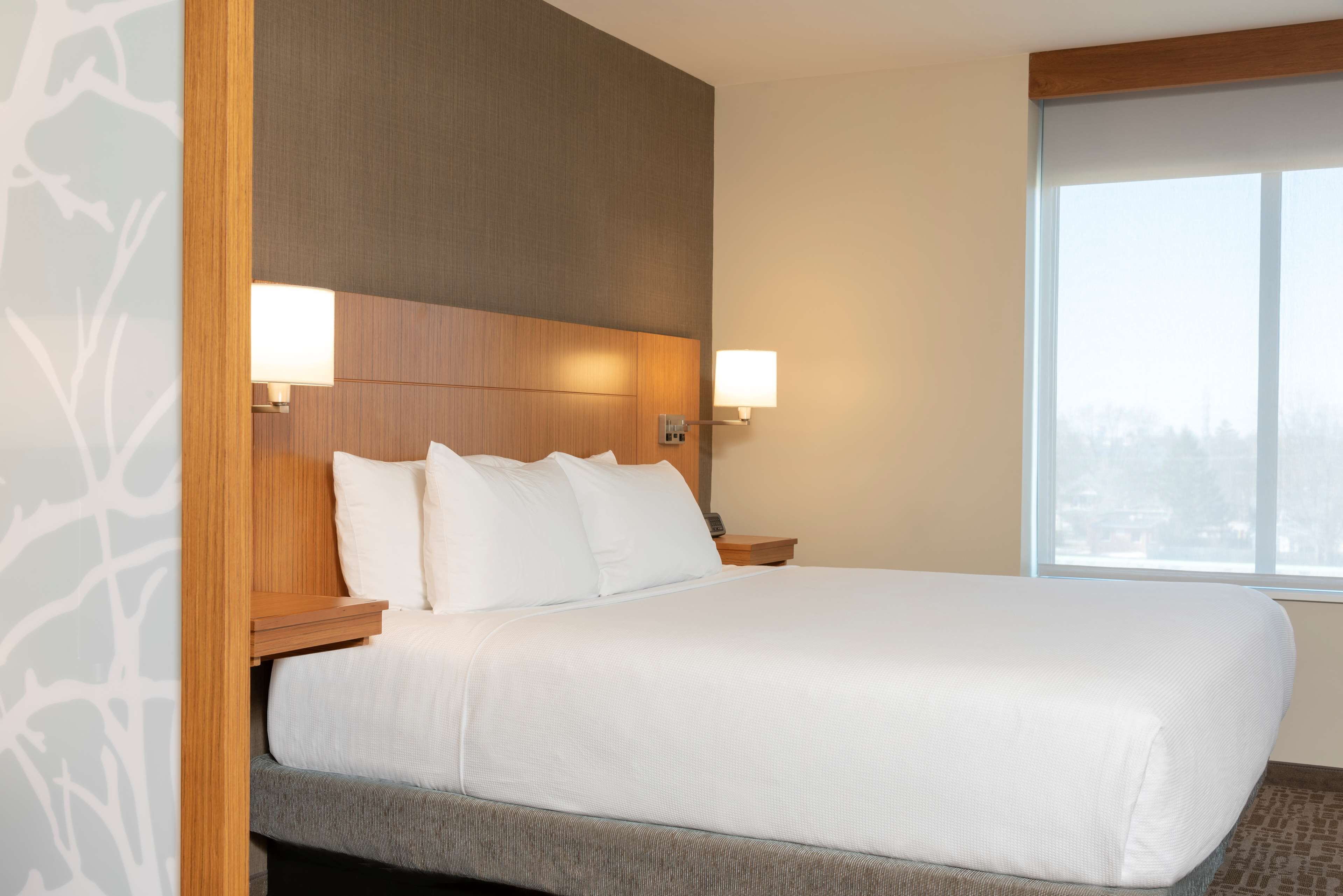 A hotel room with a large bed, wooden headboard, two bedside lamps, and a window with a view.