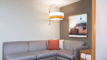 Una sala de estar moderna con un sofá seccional gris, un reposapiés marrón, una lámpara de pared y un cuadro enmarcado de un edificio.