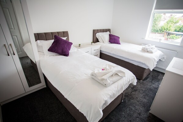 A hotel room with two beds, white bedding, and purple pillows. There is a window with a view of greenery outside.