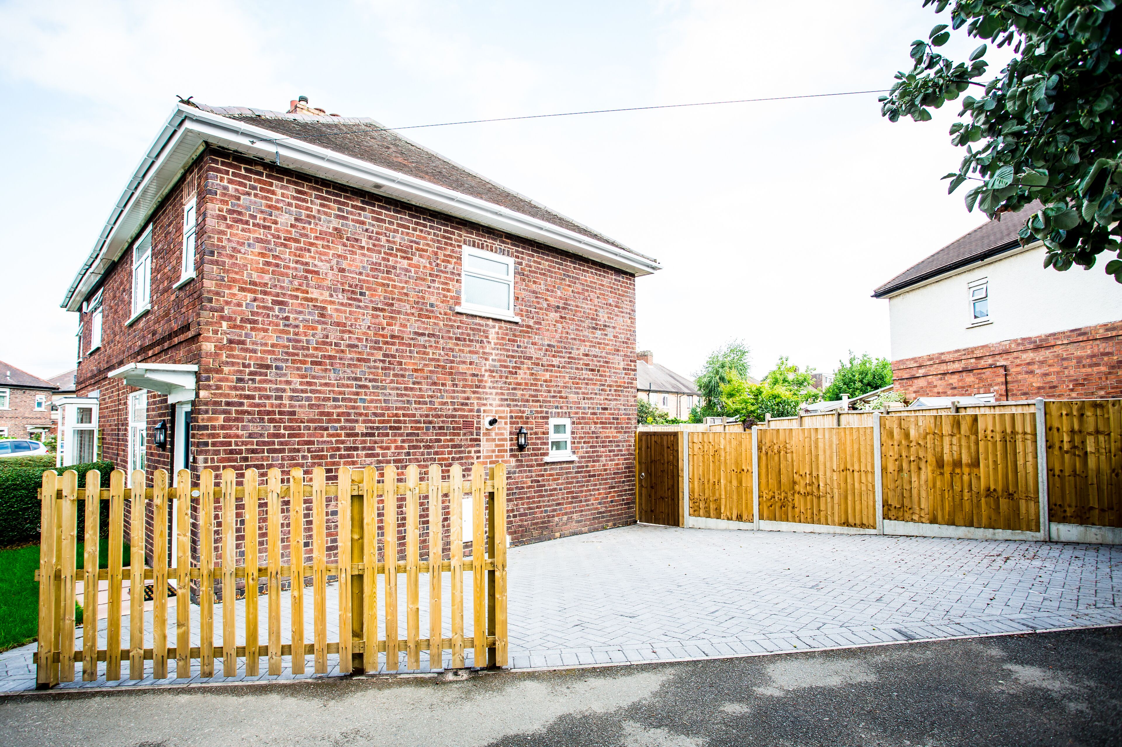 A two-story brick house with a paved driveway and a wooden gate.