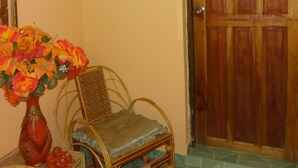Una stanza con una porta in legno, una sedia in vimini, un tavolino con un vaso di fiori e un lampadario a parete.