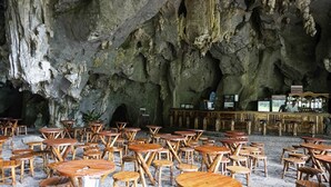 Un ristorante in una grotta con tavoli e sedie di legno disposti su un pavimento in pietra.