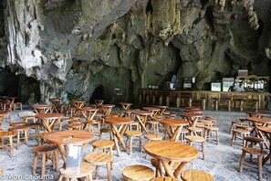 Un restaurant aménagé dans une grotte, avec des tables et des chaises en bois disposées sur un sol en pierre.