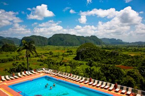 Une piscine dotée de chaises longues et offrant une vue sur des collines verdoyantes et des montagnes.