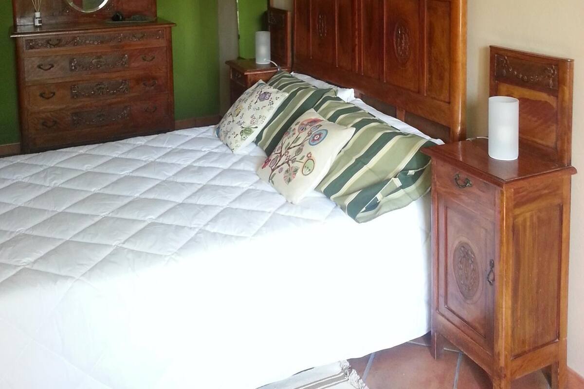 A bedroom with a wooden bed, a dresser, a mirror, and a green wall.