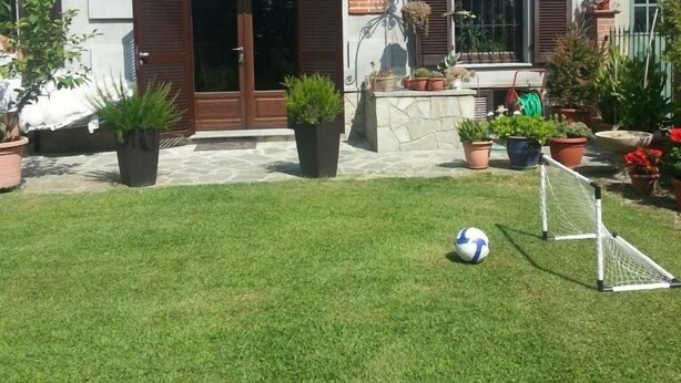 A two-story building with a brick facade, large arched windows, and a small garden area with a soccer goal.