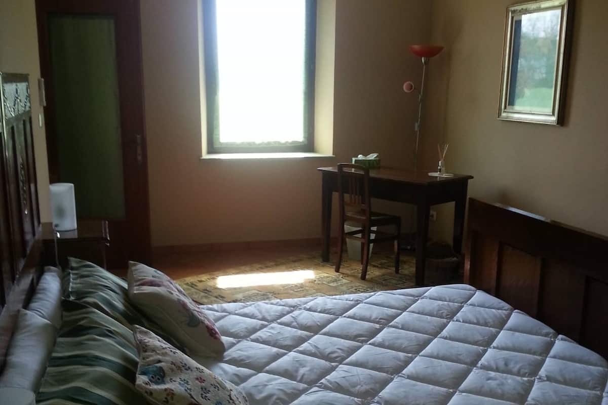 A bedroom with a large bed, a desk, and a window.
