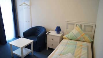 Ein Hotelzimmer mit Bett, Sessel, kleinem Tisch, Nachttisch mit Lampe und einer Garderobe.