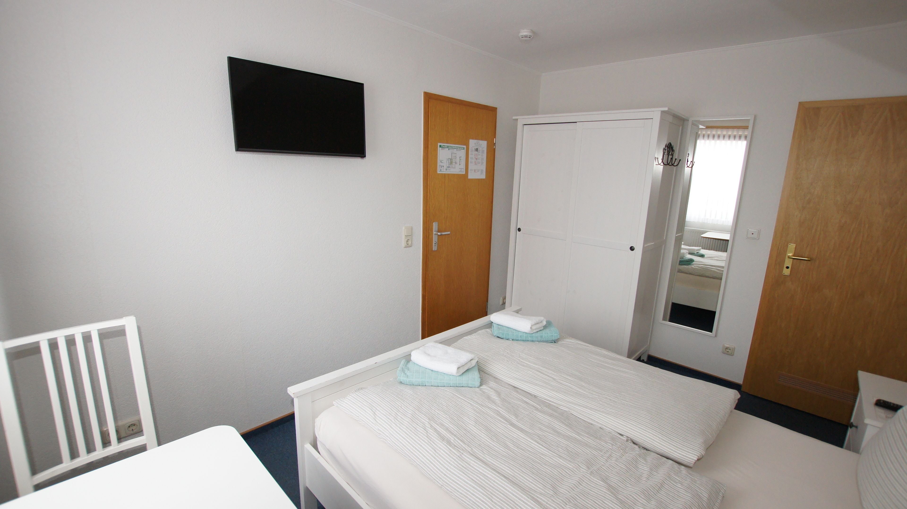 A hotel room with a bed, a TV mounted on the wall, and two doors.