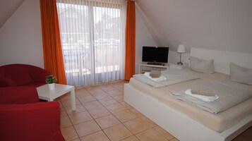 Una habitación de hotel moderna con una cama, un televisor, una mesita con una planta y una silla roja.