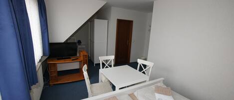 A small, tidy room with a bed, a desk with a television, a chair, and a wardrobe.