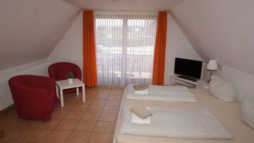 A small, triangular room with a bed, a red chair, a small table with a plant, a TV, and a lamp.