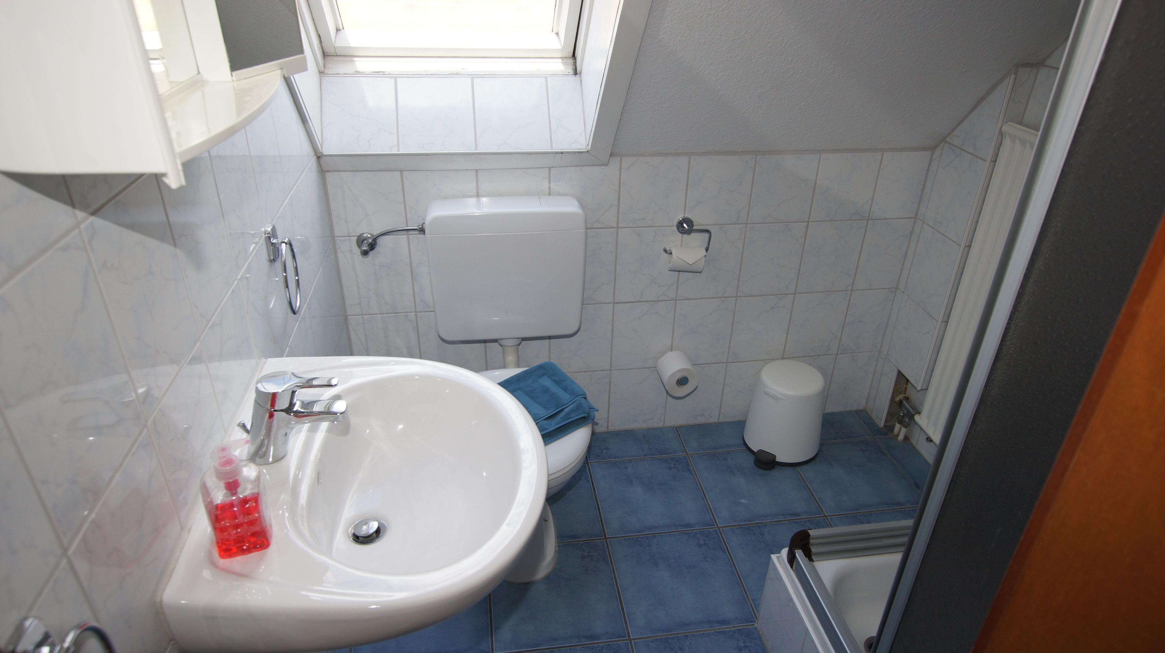 Une salle de bain avec un lavabo blanc, des carreaux bleus, des toilettes et une fenêtre.