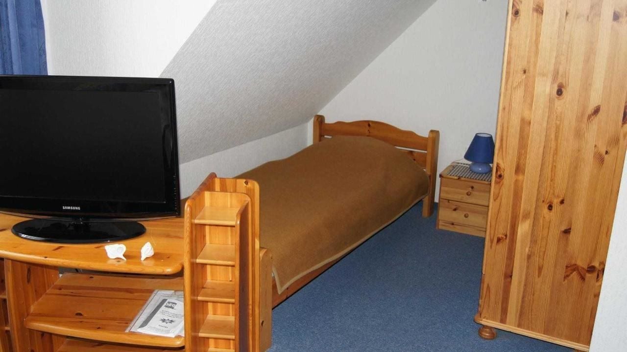 A small, single-bed room with a wooden desk and a television.