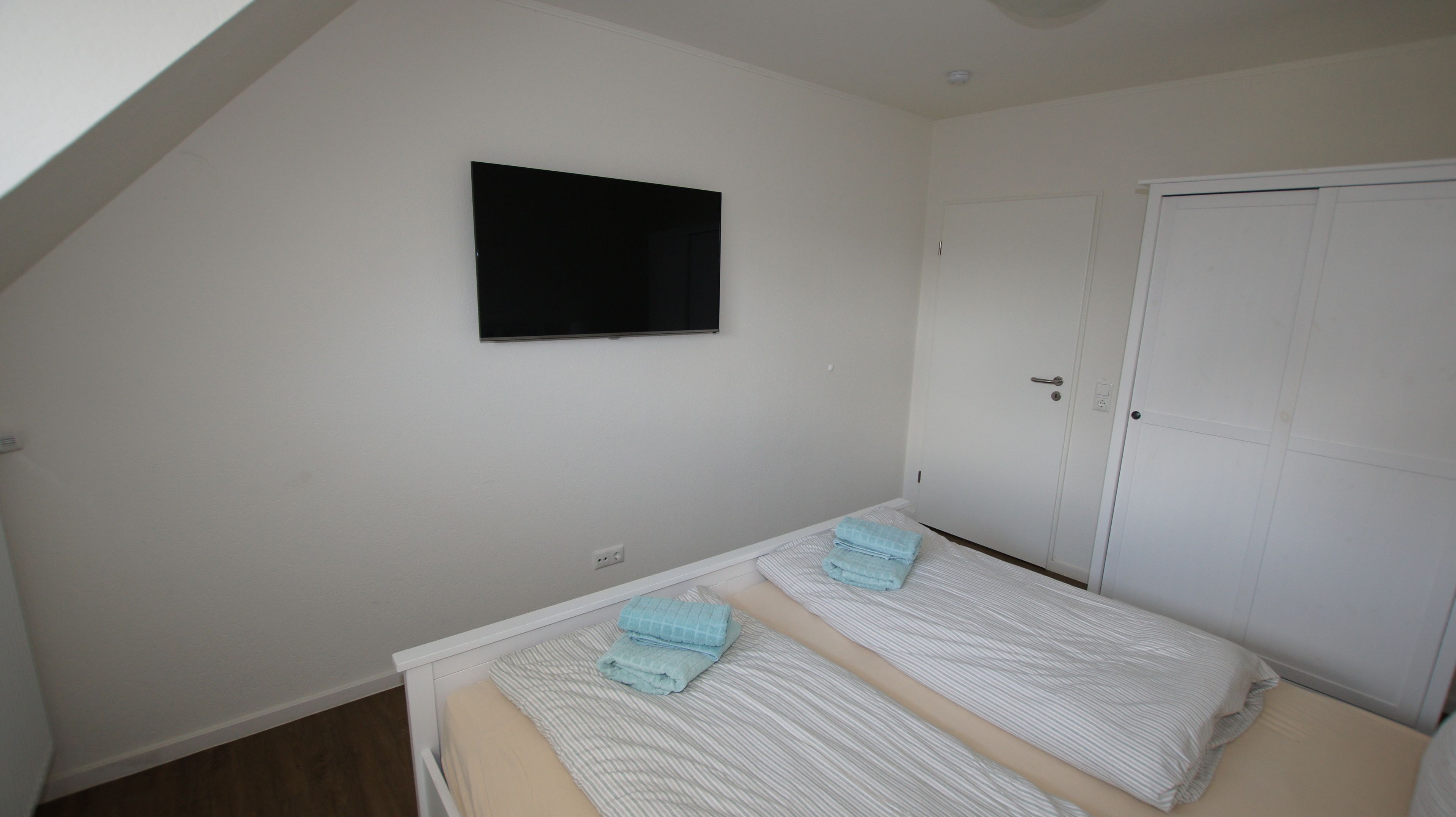 A small, clean room with two beds, a white door, and a mounted TV.