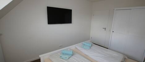 A small, clean room with two beds, a white door, and a mounted TV.