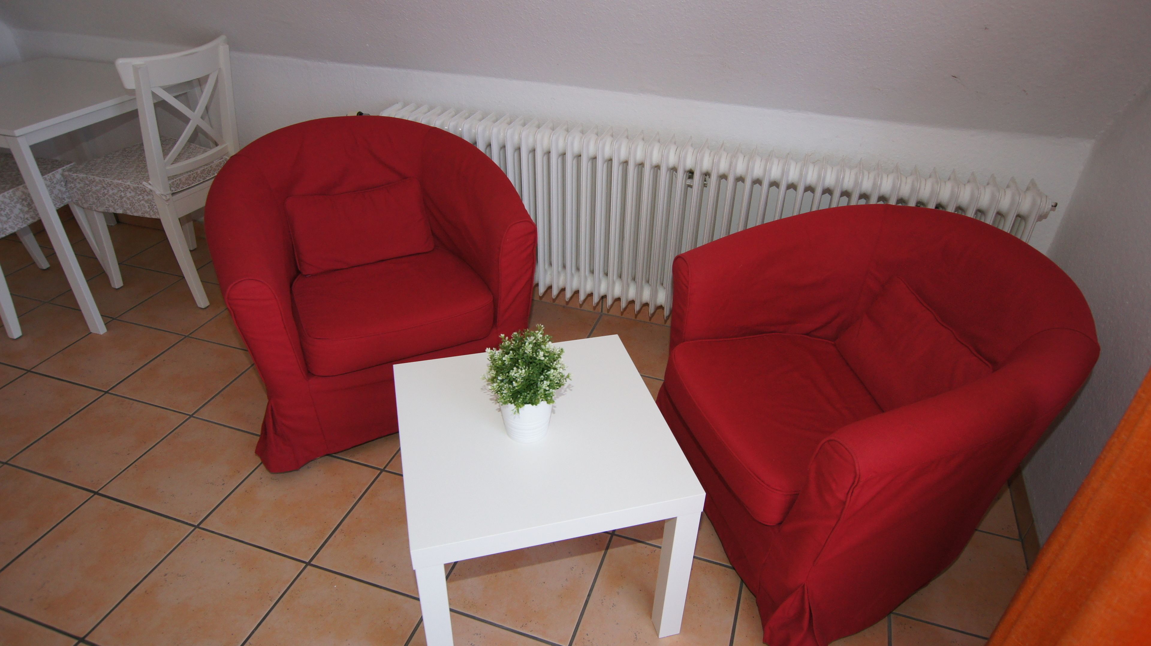 A small room with two red chairs, a white table with a potted plant, and a white radiator.