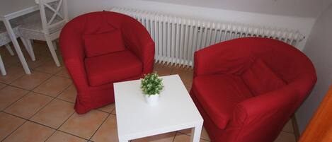 A small room with two red chairs, a white table with a potted plant, and a white radiator.