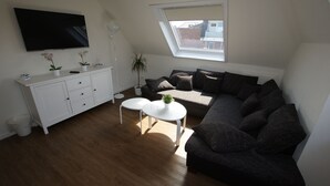 A modern living room with a sectional sofa, a white cabinet, a flat-screen TV, and a skylight. - Hotel Dorfkrug Büsum (Büsum)