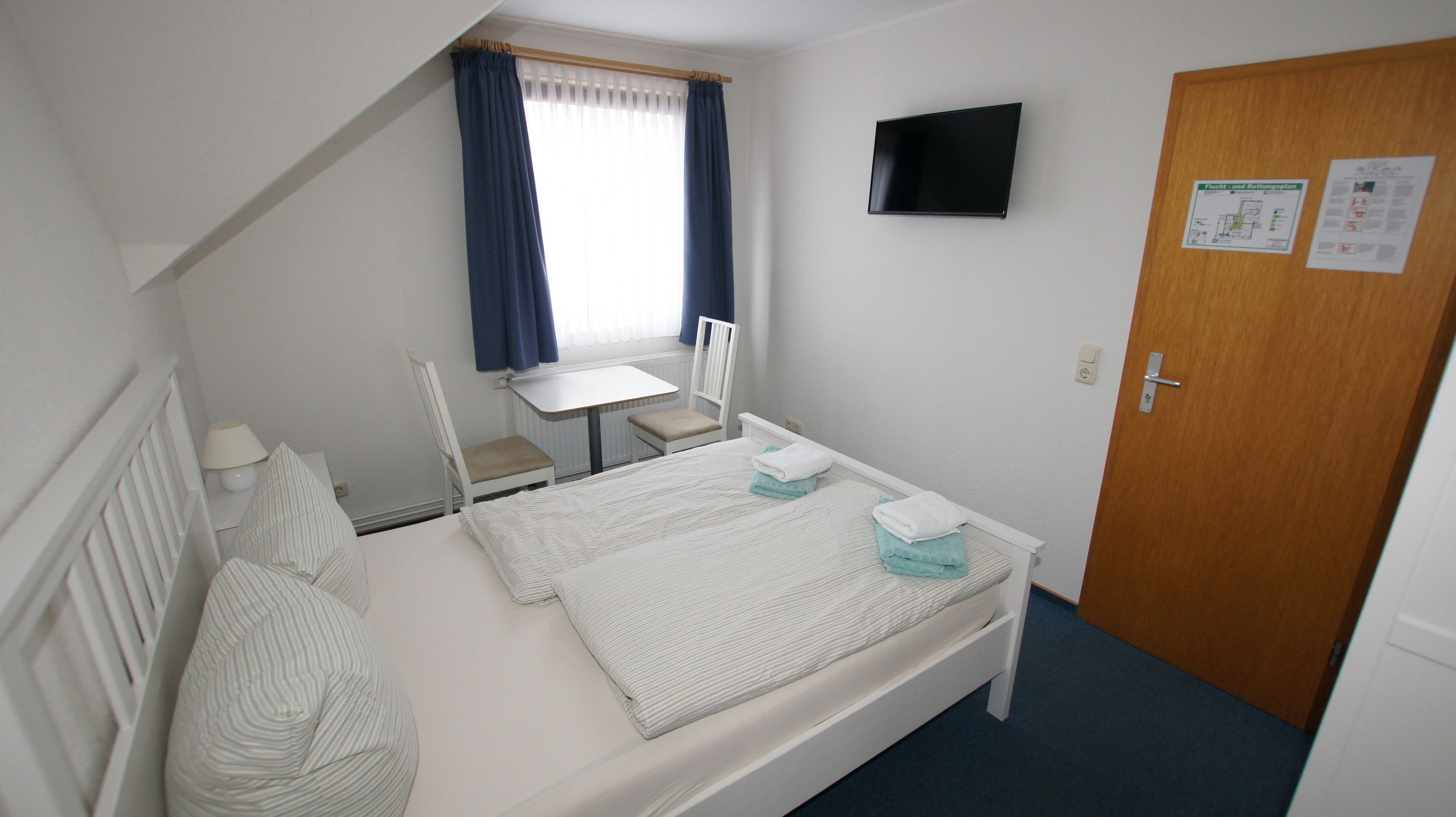 Un dormitorio pequeño y ordenado con una cama individual, una silla, una mesa y un televisor.