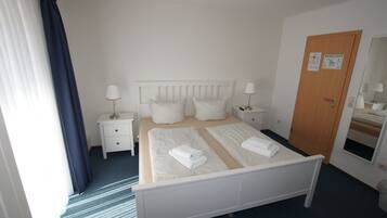 Habitación de hotel con cama, dos mesitas de noche, un tocador, una puerta de madera y un espejo.
