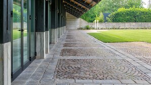 Un pasillo cubierto con pavimento de piedra y puertas de cristal que dan a un edificio.