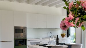 Una cocina moderna con armarios blancos, horno empotrado y zona de comedor con mesa y sillas de madera.