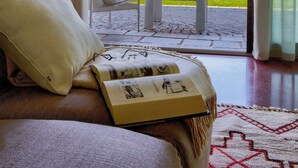 Una habitación moderna con un ventanal grande, una cama, una zona de lectura y vistas a un jardín y un edificio.