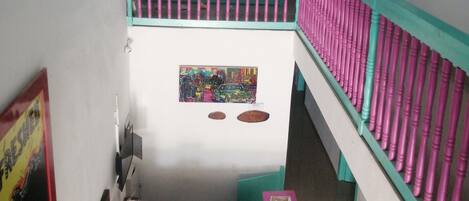 A multi-level interior with a reception desk, teal and pink railings, and a ceiling fan.