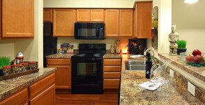 A kitchen with wooden cabinets, a black stove, a microwave, and granite countertops. - BridgeStreet at Hilliard Grand (Dublin)
