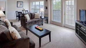 A living room with a sofa, coffee table, TV stand, and a dining area with chairs and a table. - BridgeStreet at Hilliard Grand (Dublin)