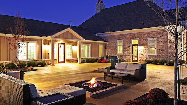 A well-lit outdoor patio area with a fire pit, seating, and a stone building with a chimney. - BridgeStreet at Hilliard Grand (Dublin)