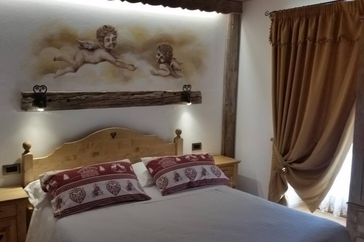 Un dormitorio con cama de madera, dos almohadas, una mesita de noche y un estante en la pared con un objeto decorativo.