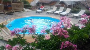 Una piscina rodeada de sillas de descanso y sombrillas, con una terraza de madera y vistas a casas al fondo.
